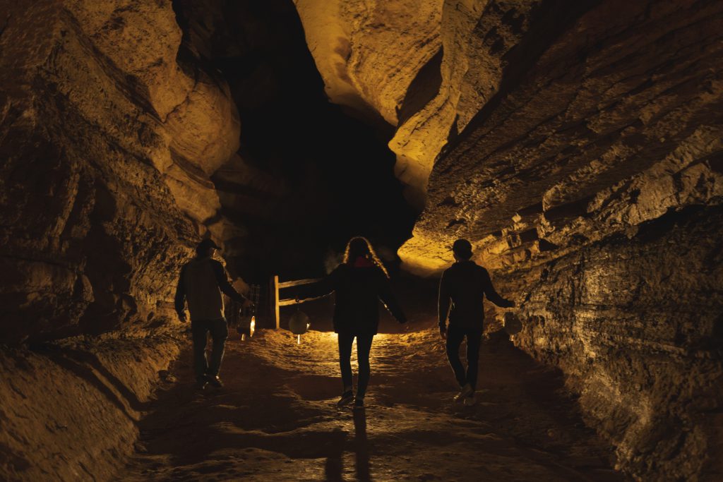 three adults walking into Manitou Springs cavern with lanterns